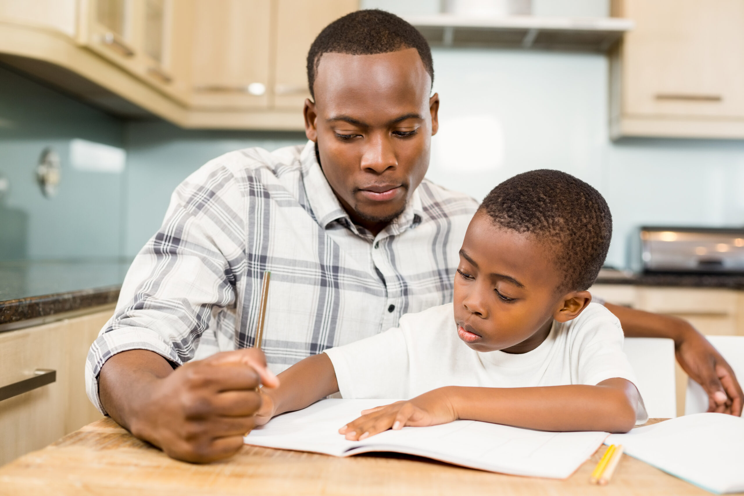 Father-helping-son-with-homework-in-kitchen-scaled